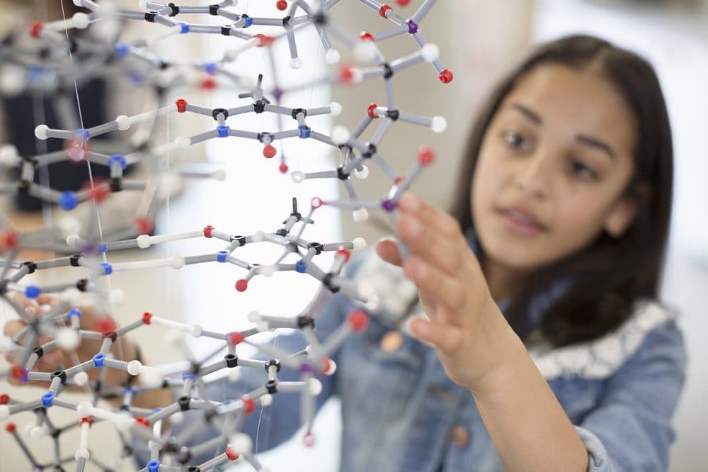 Girl student examining and touching molecular structure in classroom