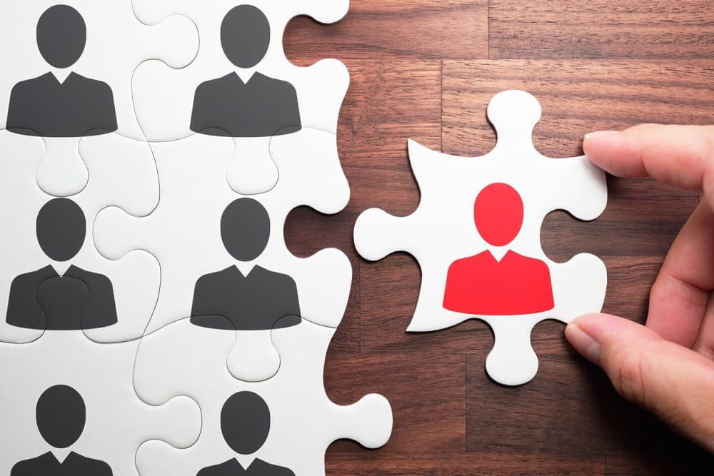 Selecting person for the job. Assembling jigsaw puzzle on wood desk.