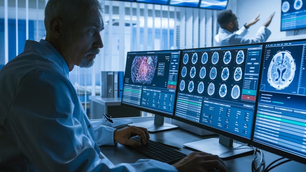 Over the Shoulder Shot of Senior Medical Scientist Working with CT Brain Scan Images on a Personal Computer in Laboratory. Neurologists in Research Center Work on Brain Tumor Cure. (Over the Shoulder Shot of Senior Medical Scientist Working with CT Br